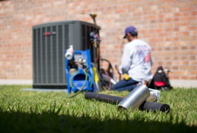 HVAC technician working on air conditioning unit next to red brick building home