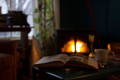 Open book open on table next to coffee cup in front of fireplace